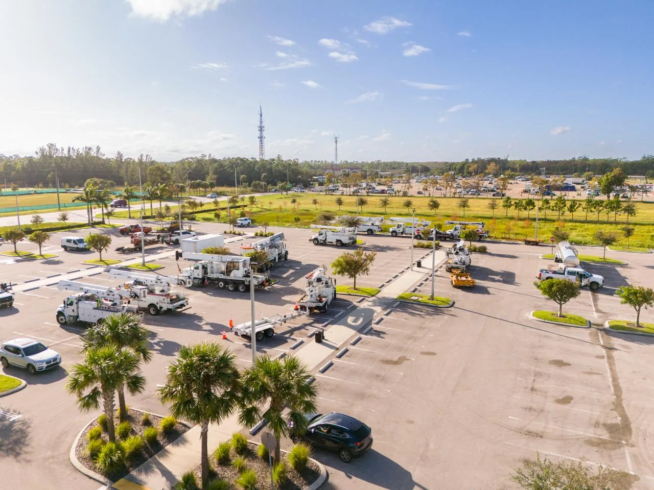 Aerial view of a utility-restoration staging lot — bucket trucks and line-crew equipment massed in a parking area near the impact zone