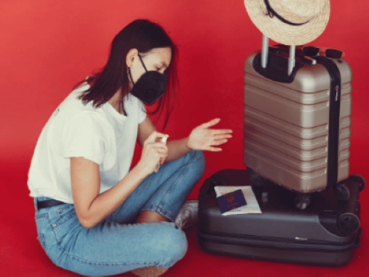 woman disinfecting hands in front of packed suitcases